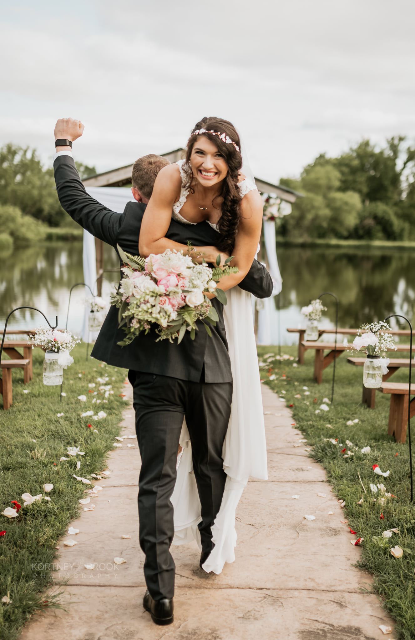 Groom carries laughing bride away from ceremony at the dock